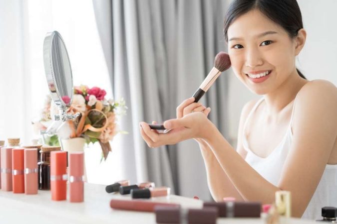 Une jeune femme applique du blush avec un pinceau lors de sa routine de maquillage.