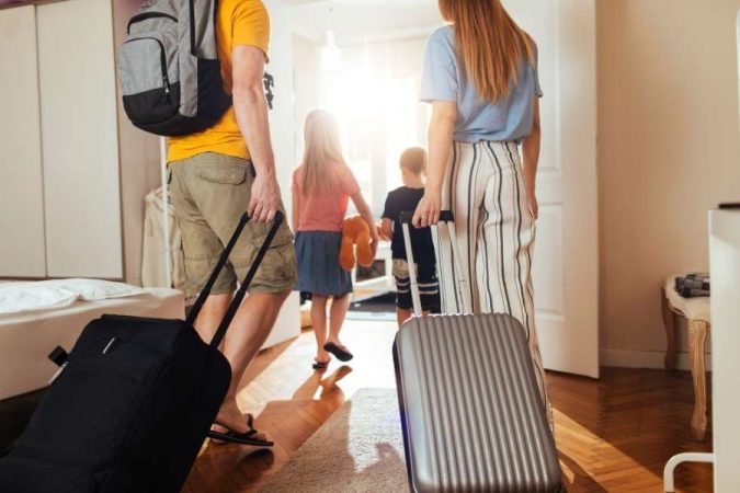 Une famille de quatre personnes quitte une chambre d'hôtel ensoleillée, prête à voyager léger.