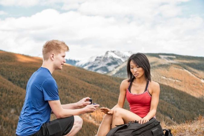 Un homme fait une demande en mariage en montagne face à une femme hésitante illustrant la peur du mariage.