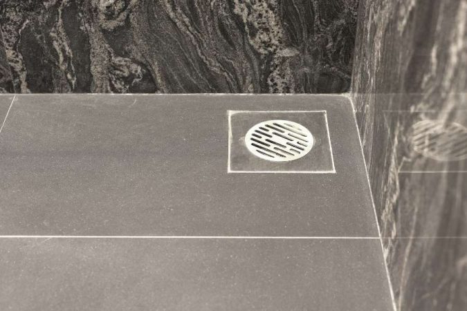 Un siphon de sol de douche en acier inoxydable élégant installé sur des carreaux en pierre sombre.