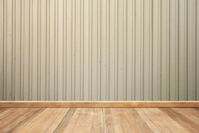 Un plancher en bois rustique aux lames larges longe un mur texturé de couleur beige.