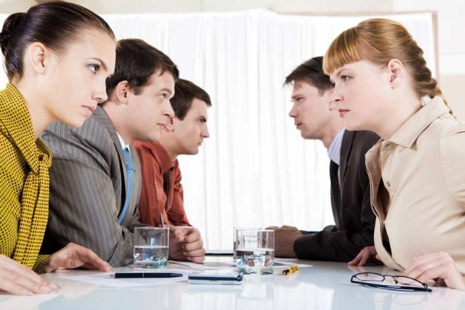 Deux camps de professionnels assis face à face lors d'une réunion tendue illustrant un conflit entre associés.